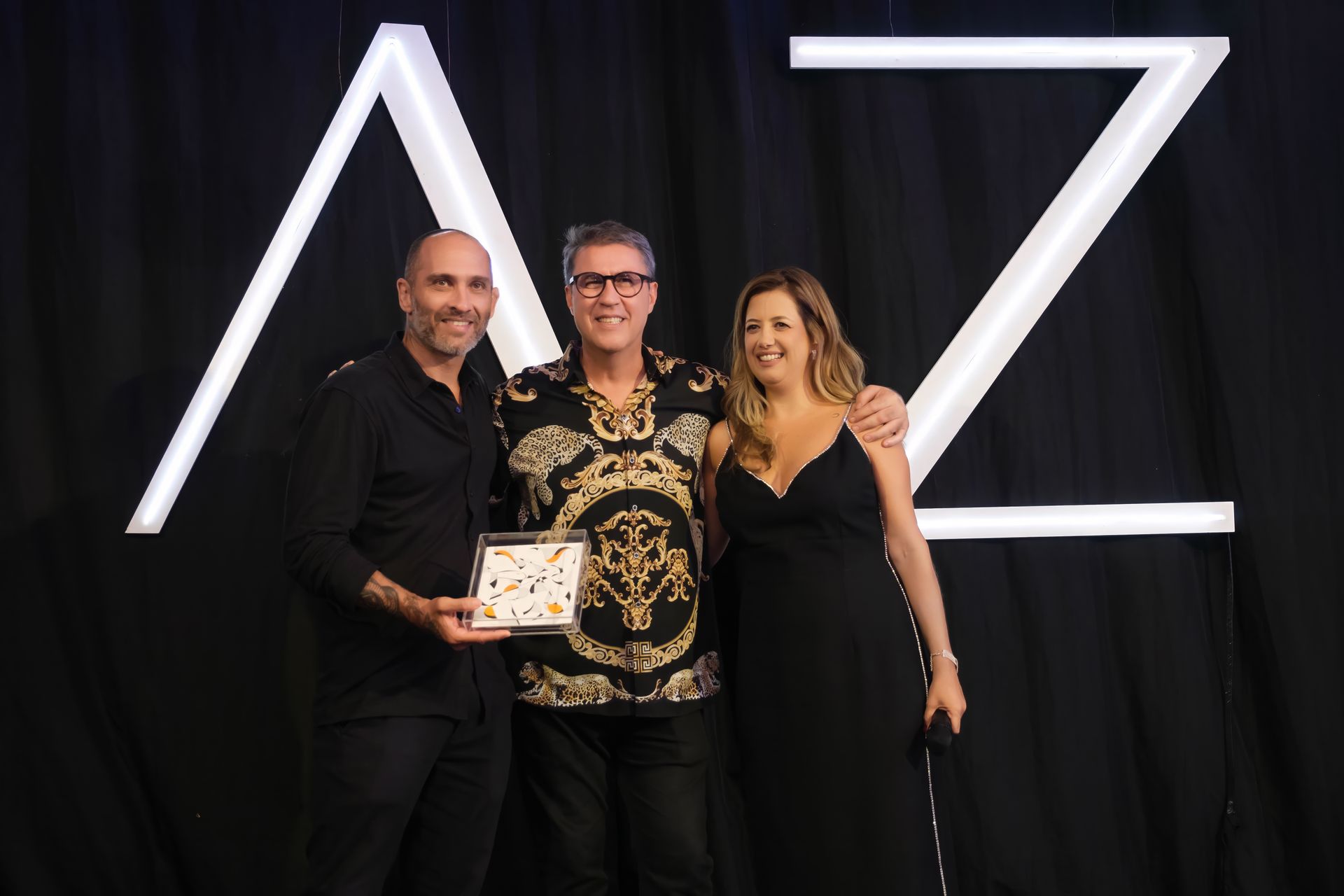 Três pessoas estão posando para uma foto em frente a uma placa que diz az.