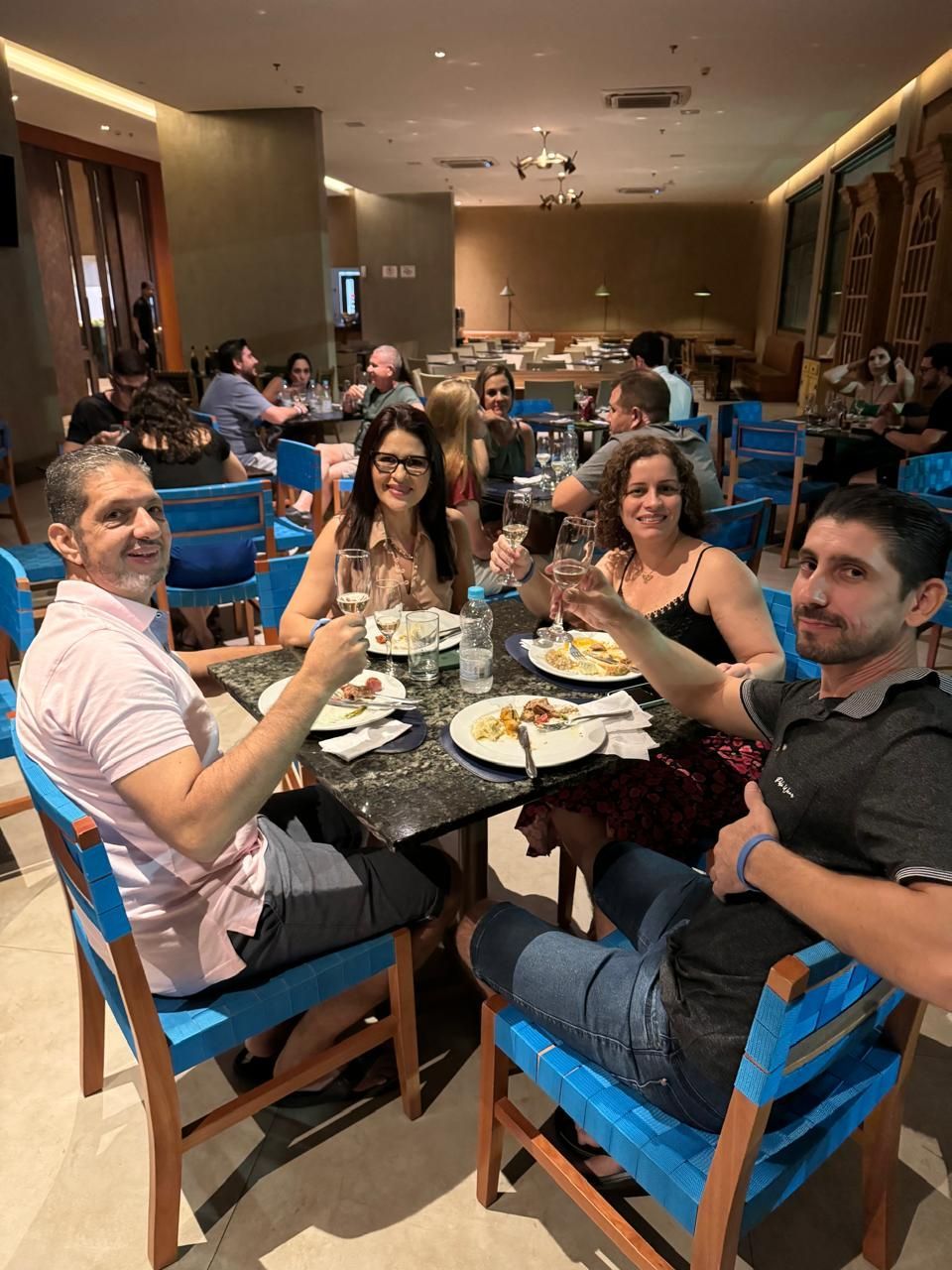 Um grupo de pessoas está sentado à mesa em um restaurante brindando com taças de vinho.