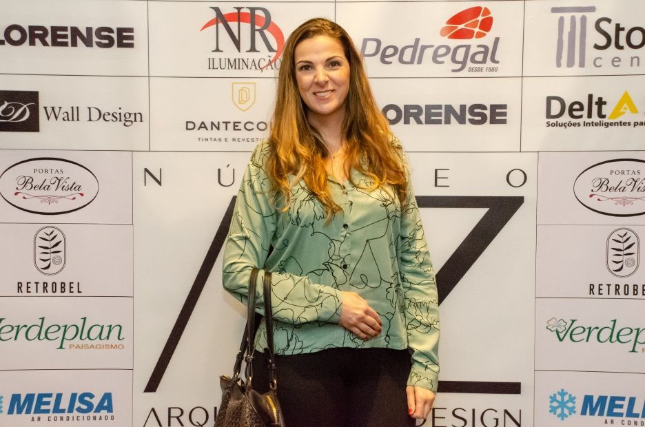 Uma mulher de camisa verde está parada em frente a uma parede com logotipos de lorense e pedregal