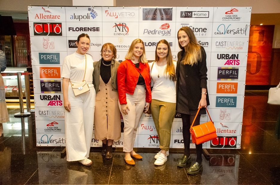 Um grupo de mulheres está posando para uma foto em frente a uma parede com logotipos.