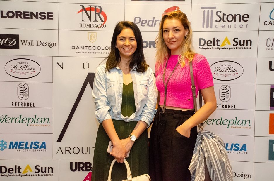 Duas mulheres estão posando para uma foto em frente a uma parede com logotipos.