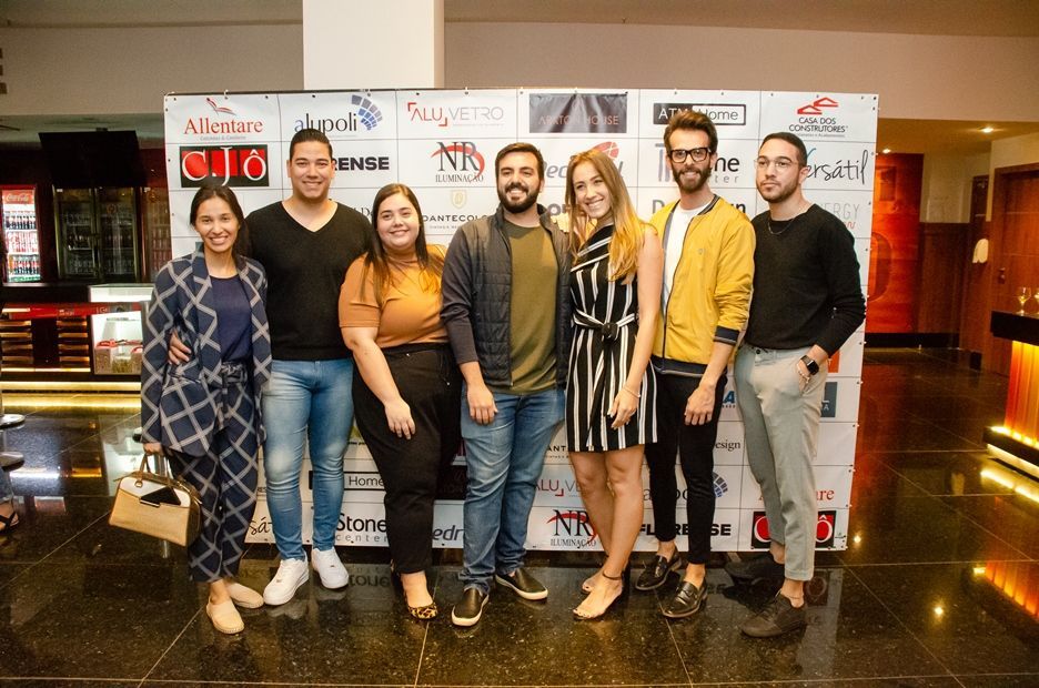 Um grupo de pessoas está posando para uma foto em frente a uma parede com logotipos.