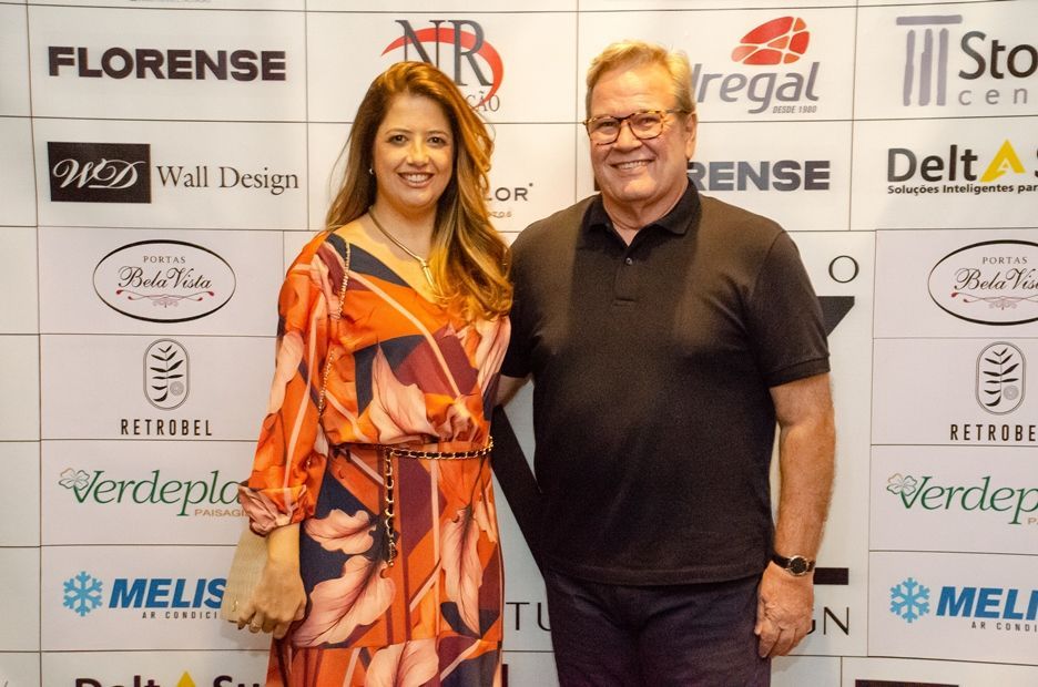 Um homem e uma mulher estão posando para uma foto em frente a uma parede com logotipos.
