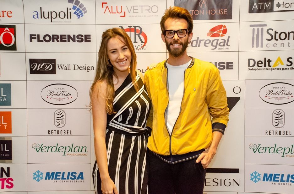 Um homem e uma mulher estão posando para uma foto em frente a uma parede de logotipos