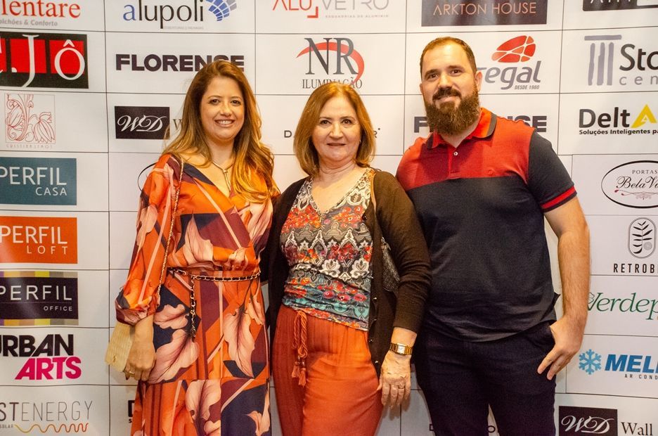 Três pessoas estão posando para uma foto em frente a uma parede com logotipos.