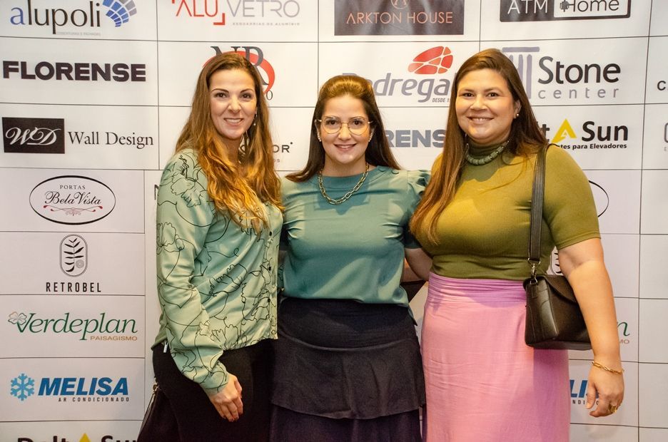 Três mulheres estão posando para uma foto em frente a uma parede com logotipos.