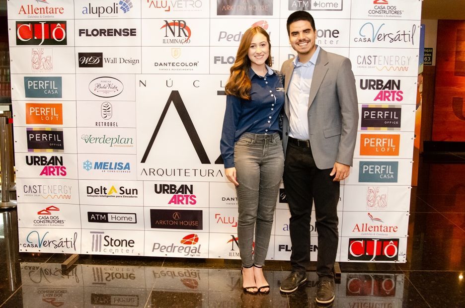 Um homem e uma mulher estão em pé em frente a uma parede coberta de logotipos.