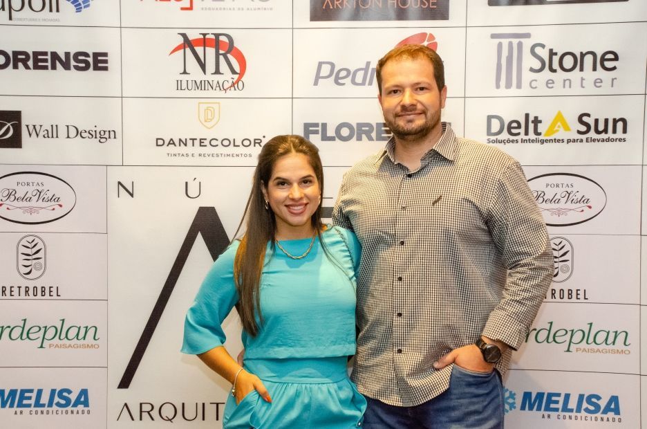 Um homem e uma mulher estão posando para uma foto em frente a uma parede com logotipos.