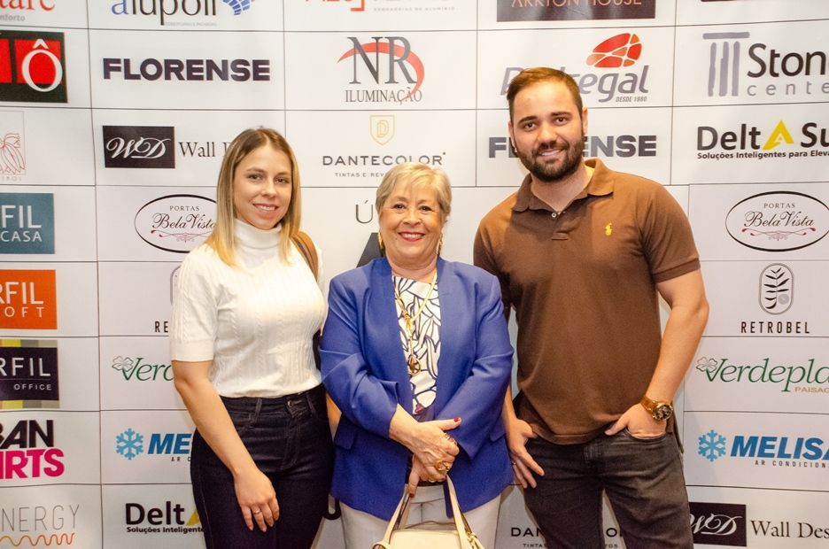 Três pessoas estão posando para uma foto em frente a uma parede com logotipos.