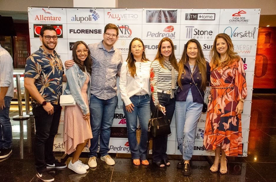 Um grupo de pessoas está posando para uma foto em frente a uma parede com logotipos.