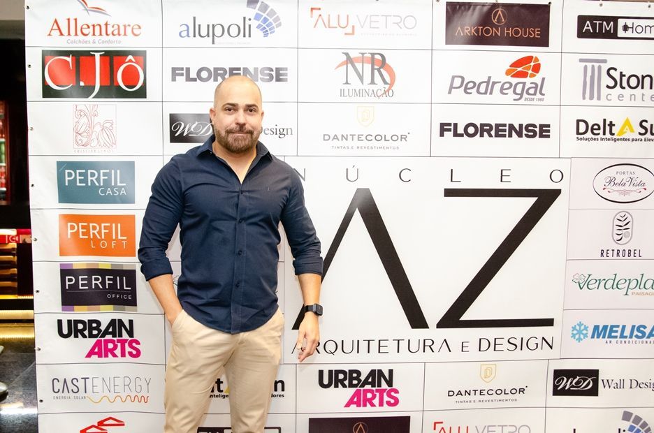 Um homem careca está parado em frente a uma parede com vários logotipos.