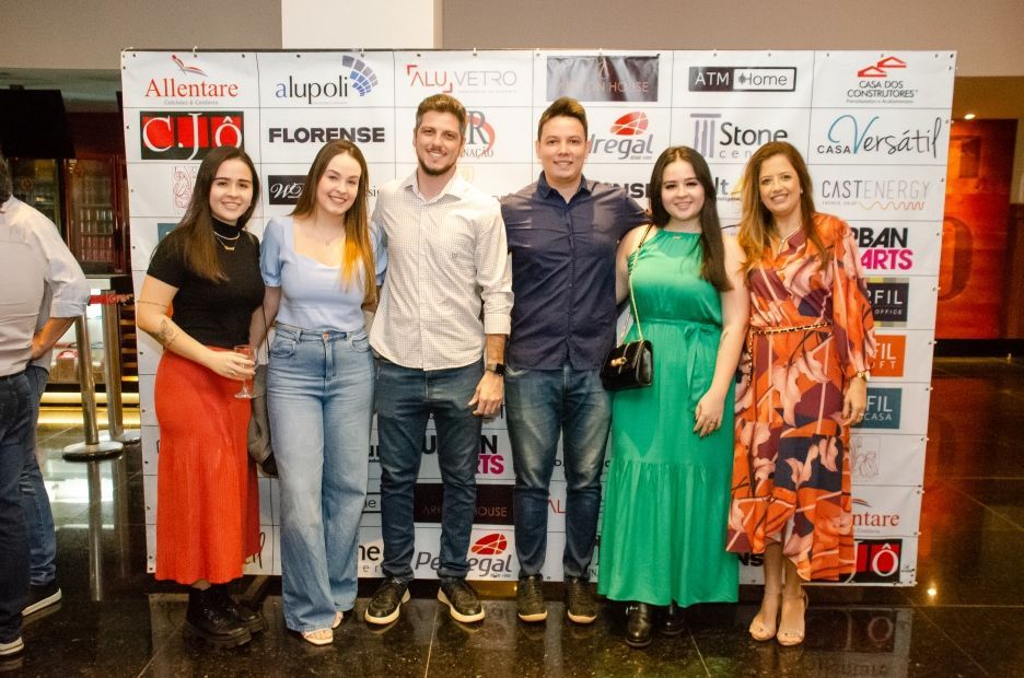 Um grupo de pessoas está posando para uma foto em frente a uma parede com logotipos.