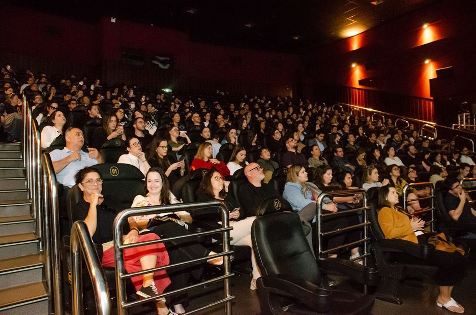 Um grande grupo de pessoas está sentado em um cinema assistindo a um filme.