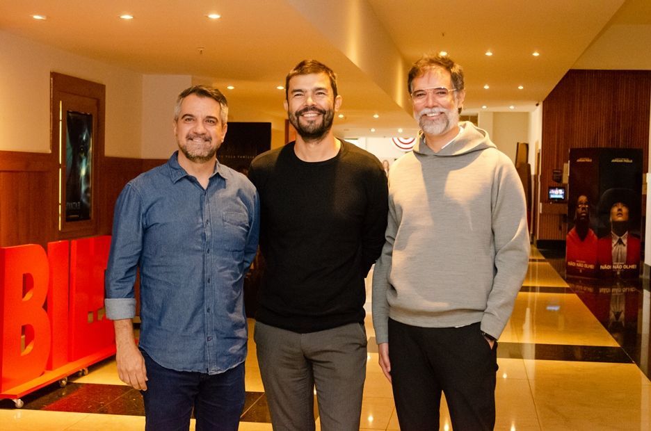 Três homens estão parados um ao lado do outro em um corredor.