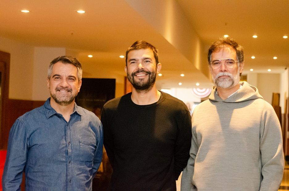 Três homens estão posando para uma foto juntos em um corredor.