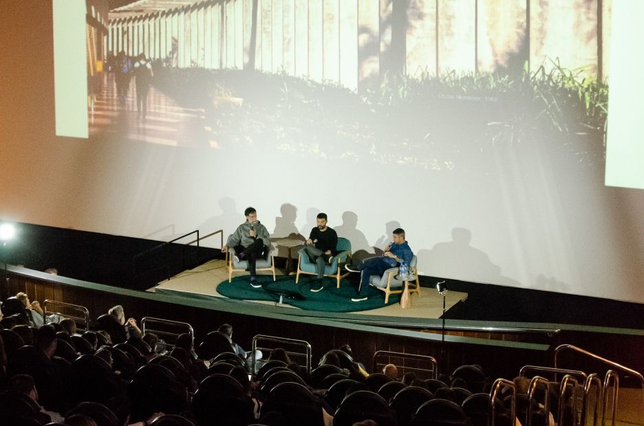 Um grupo de pessoas está sentado em um palco em frente a uma tela grande.