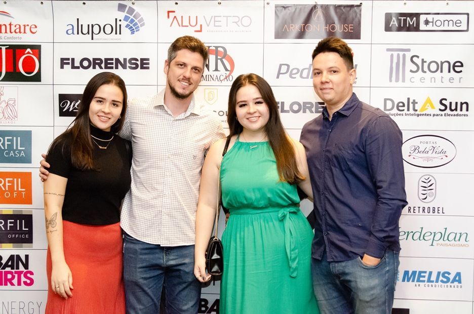 Um grupo de pessoas está posando para uma foto em frente a uma parede com logotipos.