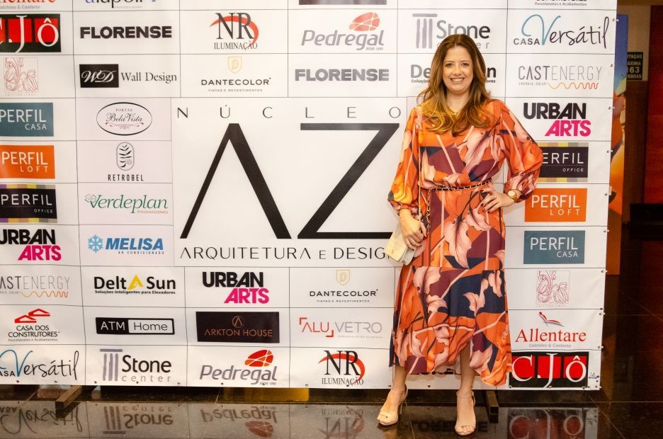 Uma mulher de vestido está parada em frente a uma parede de logotipos.