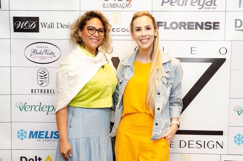 Duas mulheres estão posando para uma foto em frente a uma parede com logotipos.