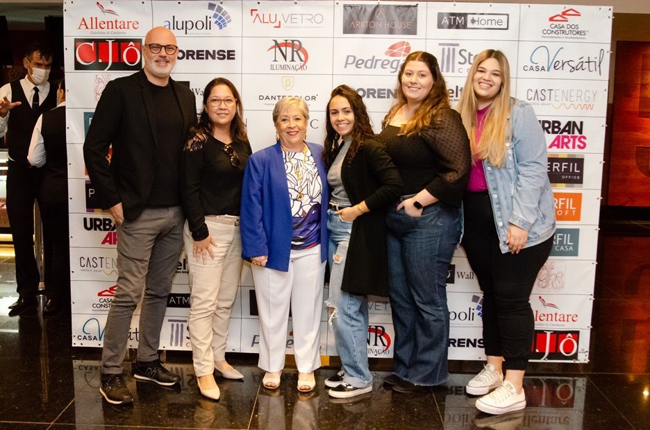 Um grupo de pessoas está posando para uma foto em frente a uma parede com logotipos.