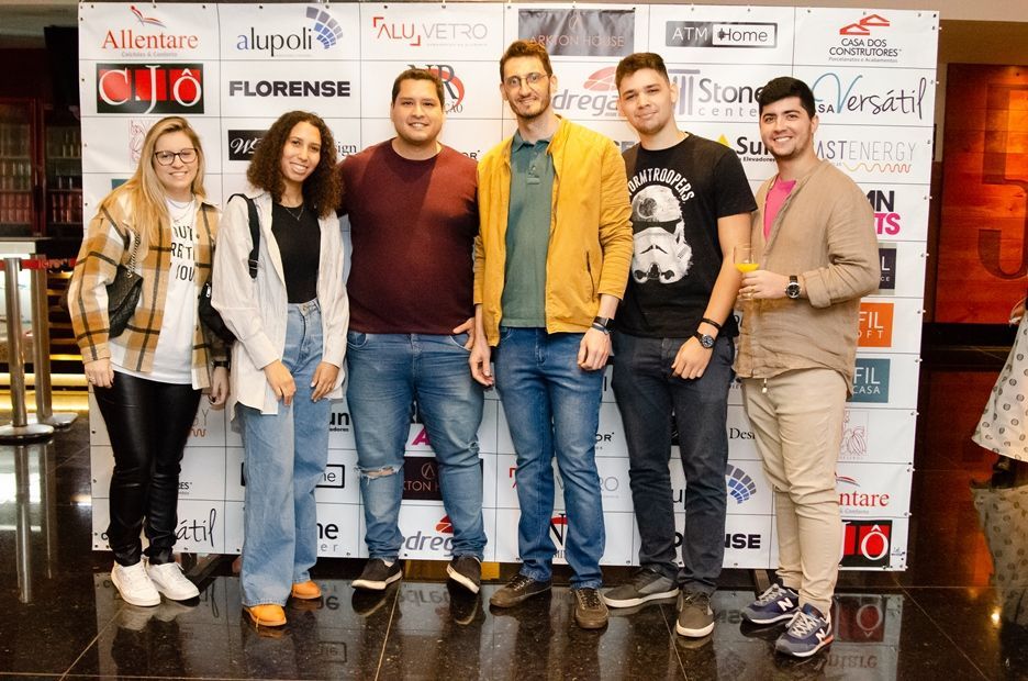 Um grupo de pessoas está posando para uma foto em frente a uma parede com logotipos.