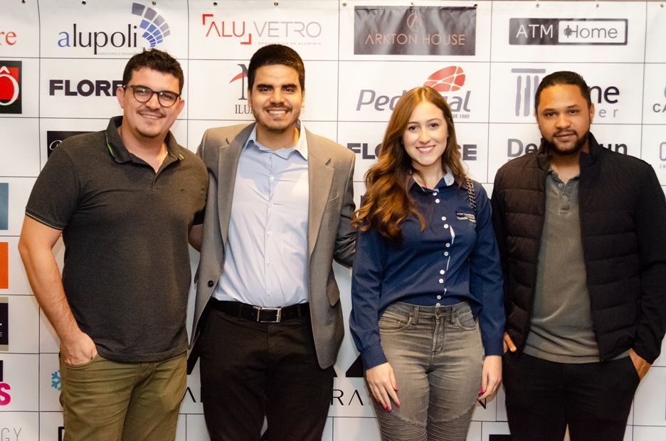 Um grupo de pessoas está posando para uma foto em frente a uma parede com logotipos de várias empresas