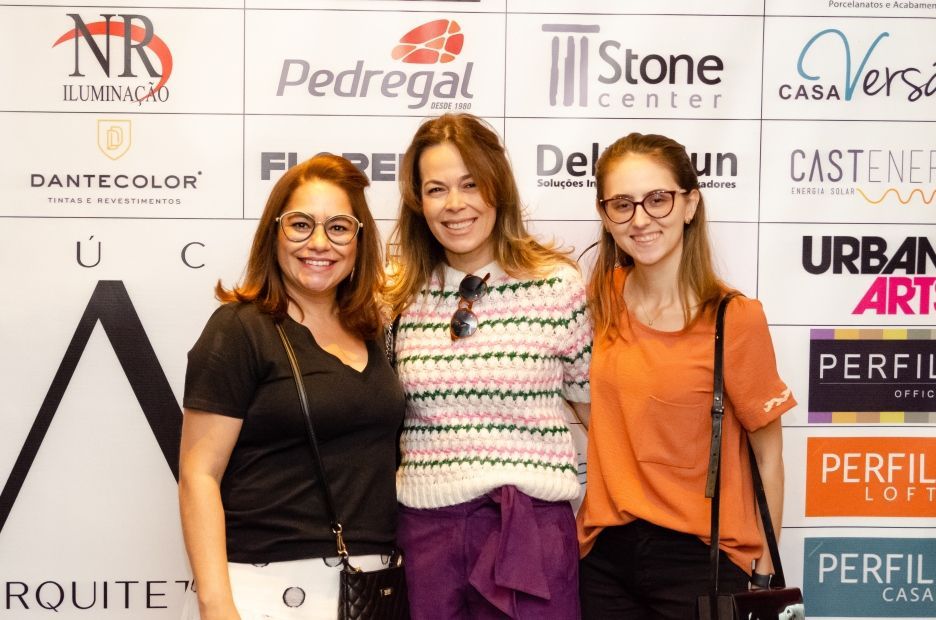 Três mulheres estão posando para uma foto em frente a uma parede com logotipos.