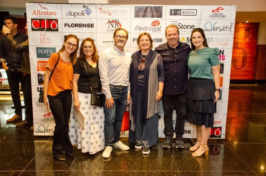 Um grupo de pessoas está posando para uma foto em frente a uma parede com logotipos.