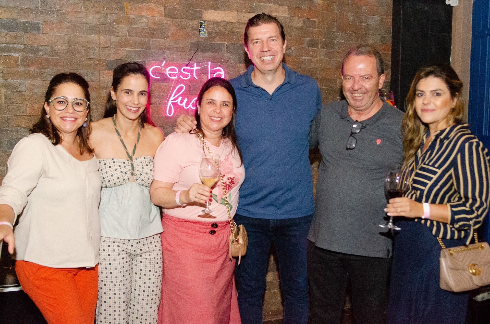 Um grupo de pessoas está posando para uma foto em frente a um letreiro de neon.