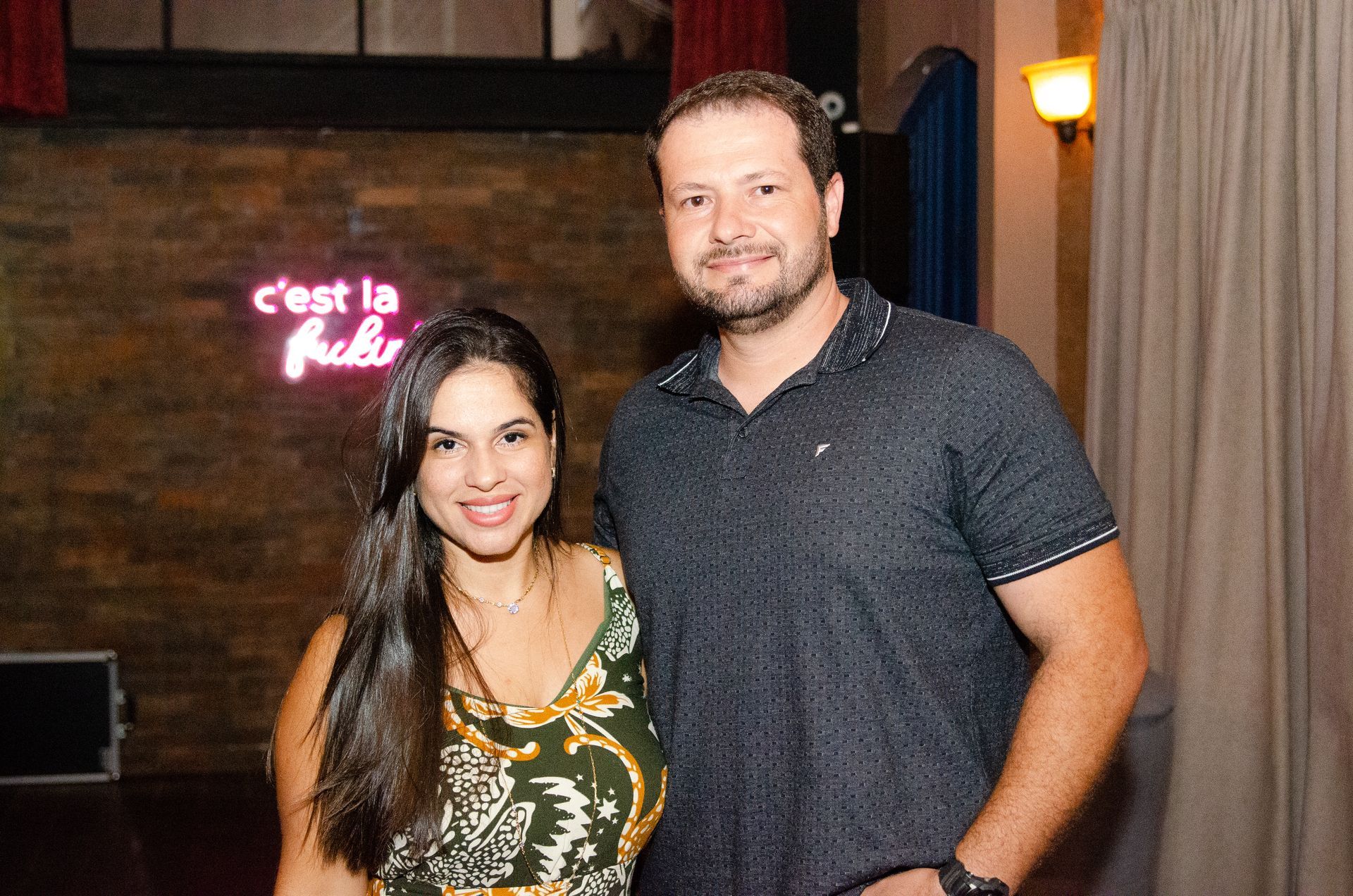 Um homem e uma mulher estão posando para uma foto em frente a um letreiro de neon.