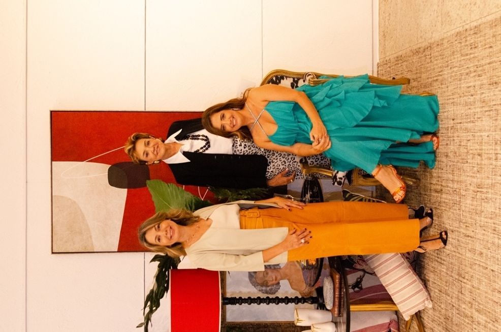 Um homem e duas mulheres estão de pé, um ao lado do outro, em frente a uma pintura.