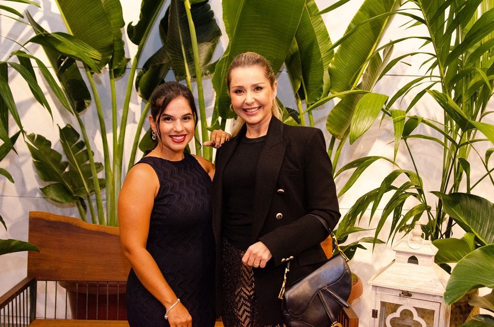 Duas mulheres estão posando para uma foto em frente a uma planta.