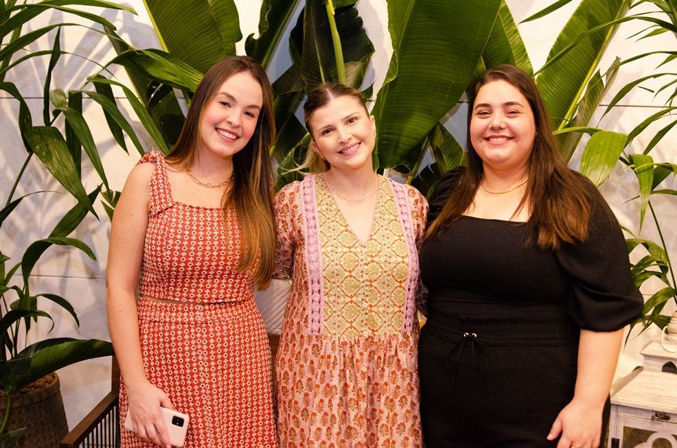 Três mulheres estão posando para uma foto em frente a uma planta.