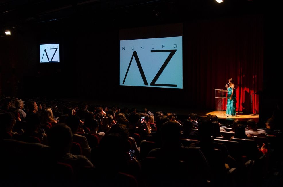 Uma mulher está em pé no palco em frente a uma tela que diz az