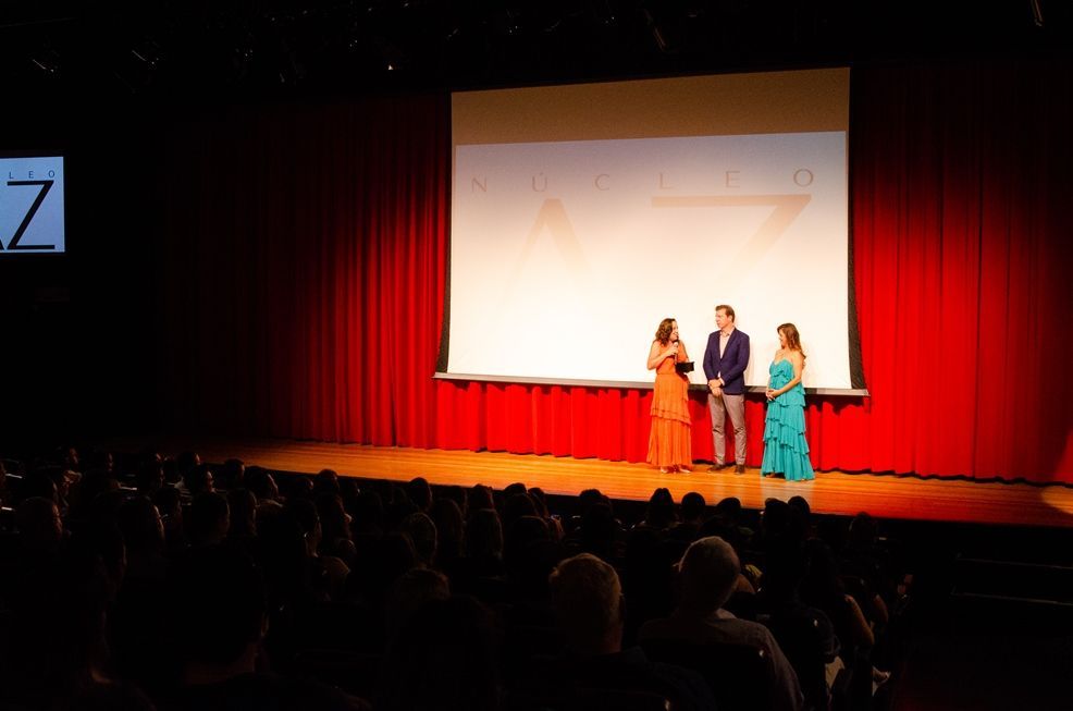 Um grupo de pessoas está em pé em um palco em frente a uma tela grande.