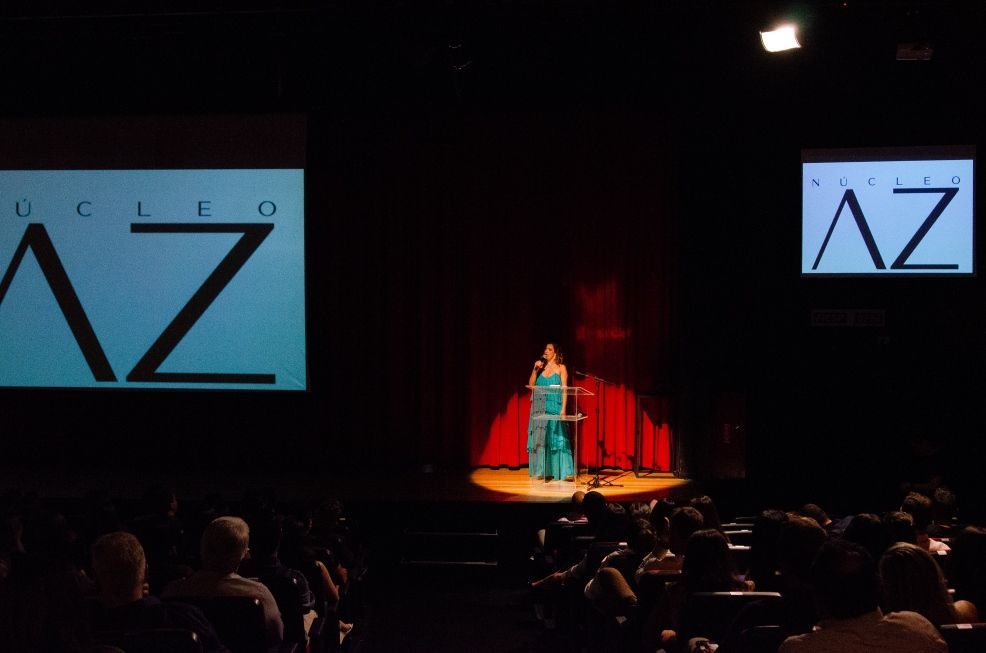 Uma mulher está em um palco em frente a uma tela que diz az