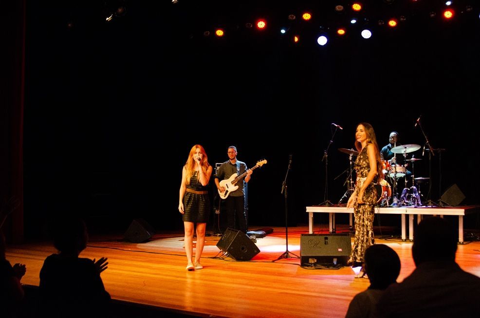 Um grupo de pessoas está em um palco cantando em microfones.