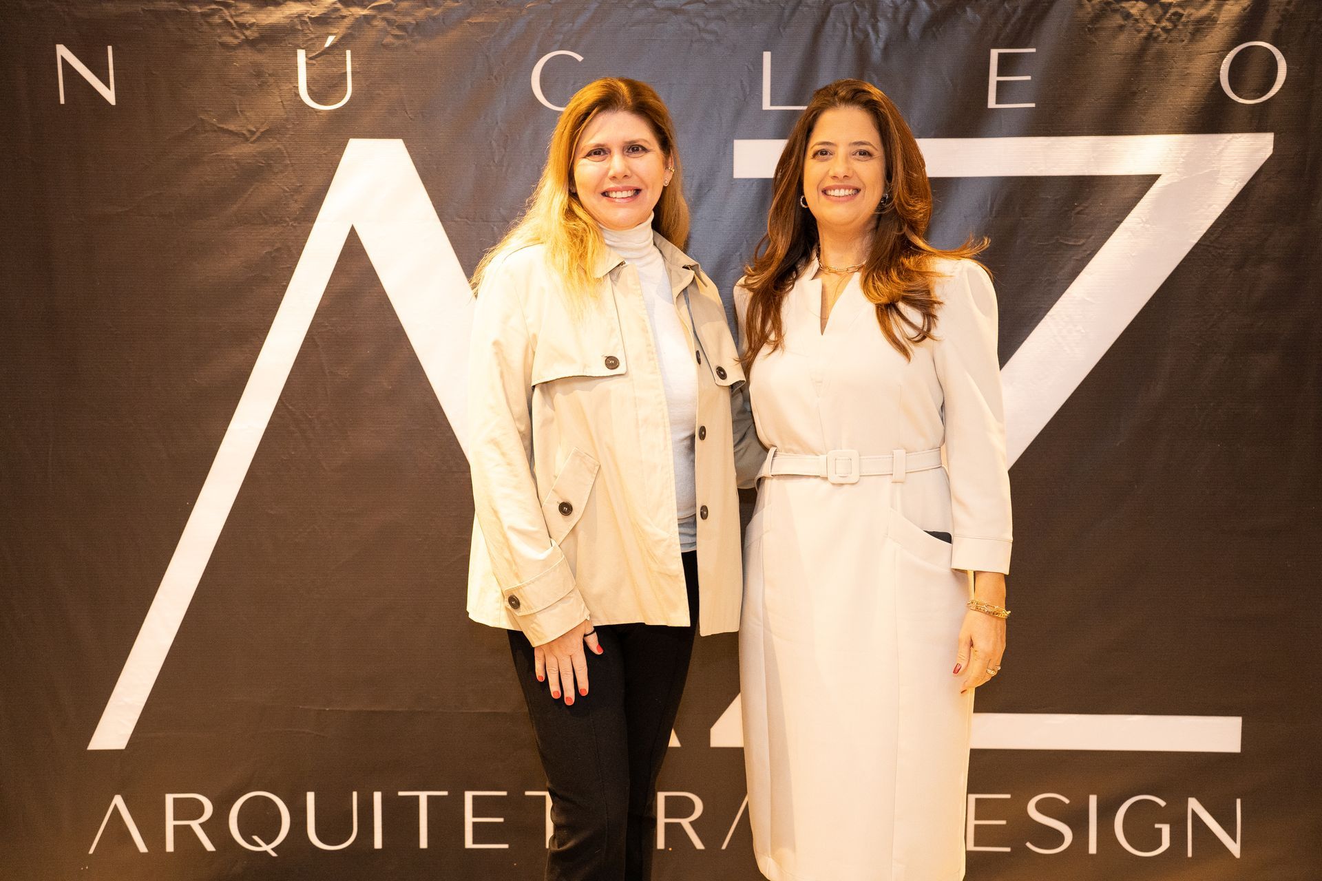 Duas mulheres posam para uma foto em frente a uma placa que diz arquiteta design