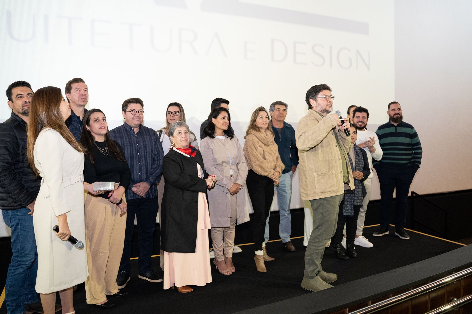 Um grupo de pessoas está em pé em um palco em frente a uma tela grande.