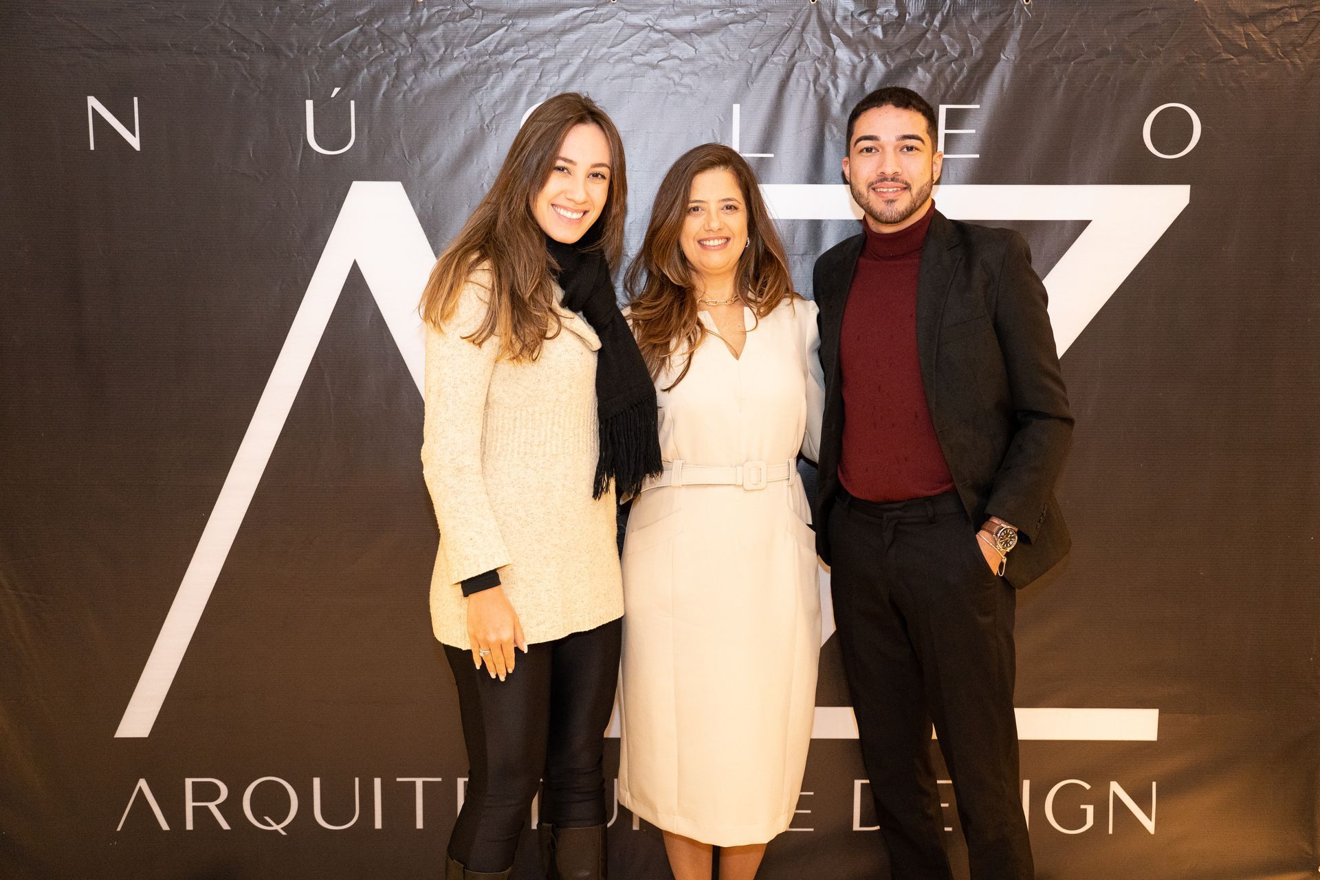 Três pessoas estão posando para uma foto em frente a uma placa que diz arquit