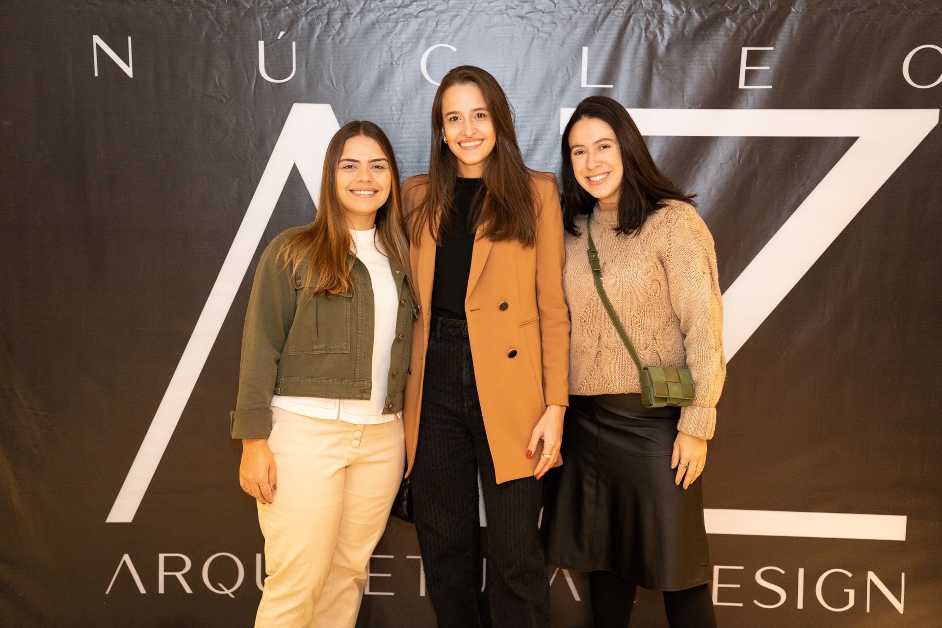 Três mulheres estão posando para uma foto em frente a uma placa.