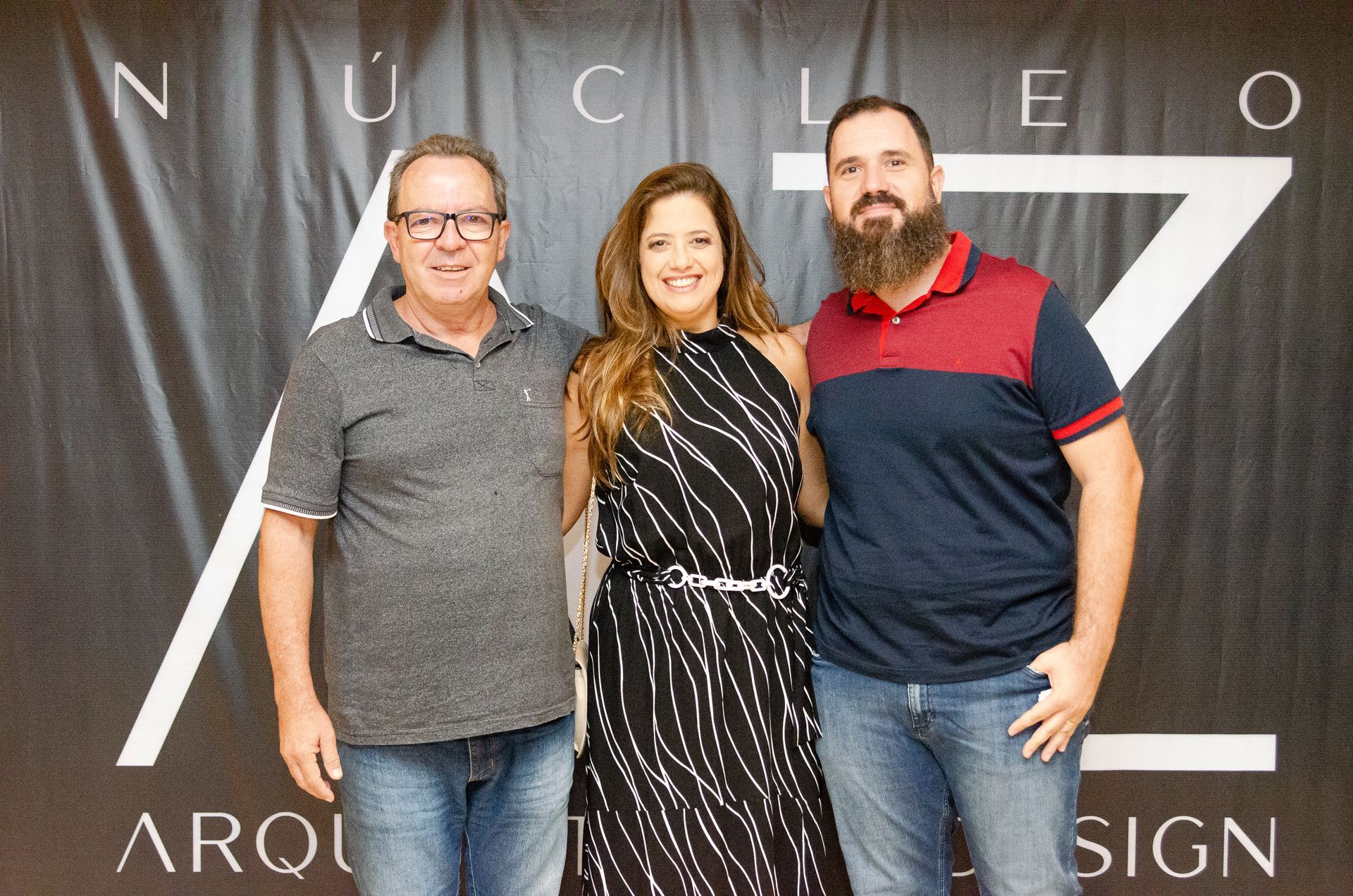 Três pessoas estão posando para uma foto em frente a uma placa que diz nucleo