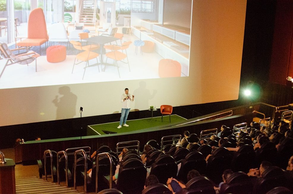 Um homem está fazendo uma apresentação em frente a uma tela grande em um auditório