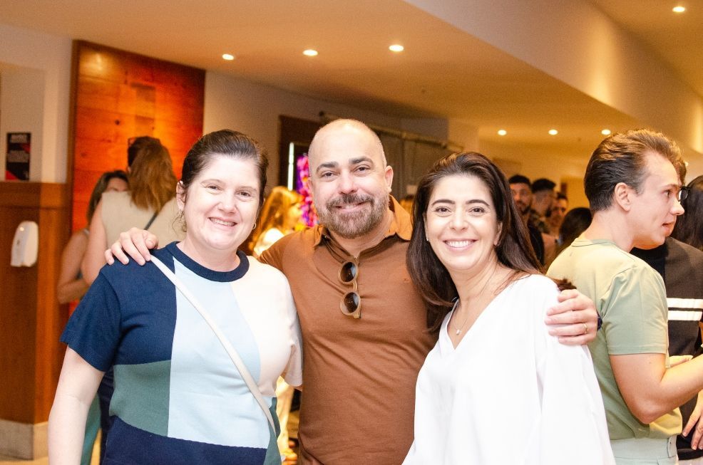 Um homem e duas mulheres estão posando para uma foto em uma sala lotada.