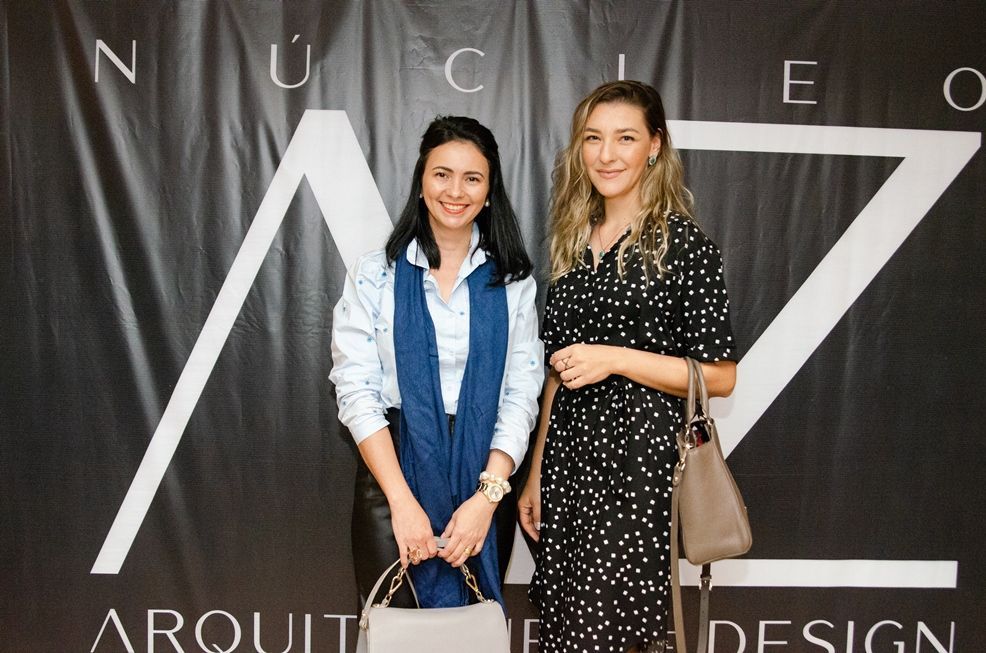 Duas mulheres posam para uma foto em frente a uma placa que diz arquitetura design