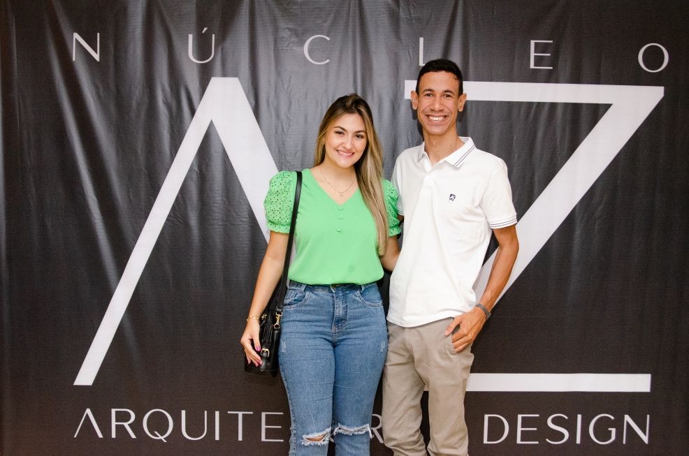 Um homem e uma mulher estão posando para uma foto em frente a uma placa que diz arquitete design.