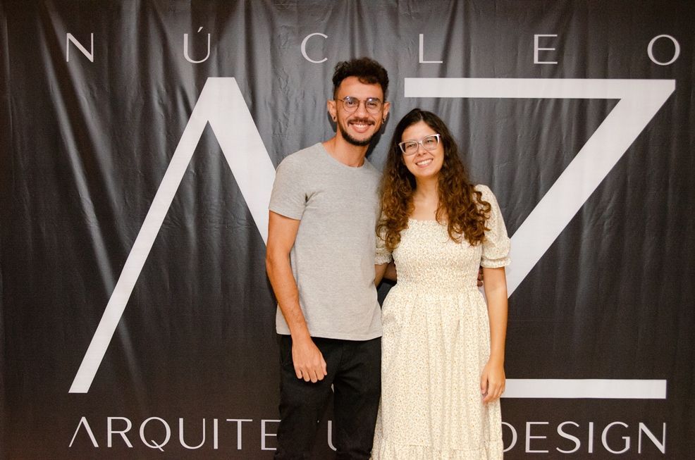 Um homem e uma mulher estão posando para uma foto em frente a uma placa que diz arquitet design