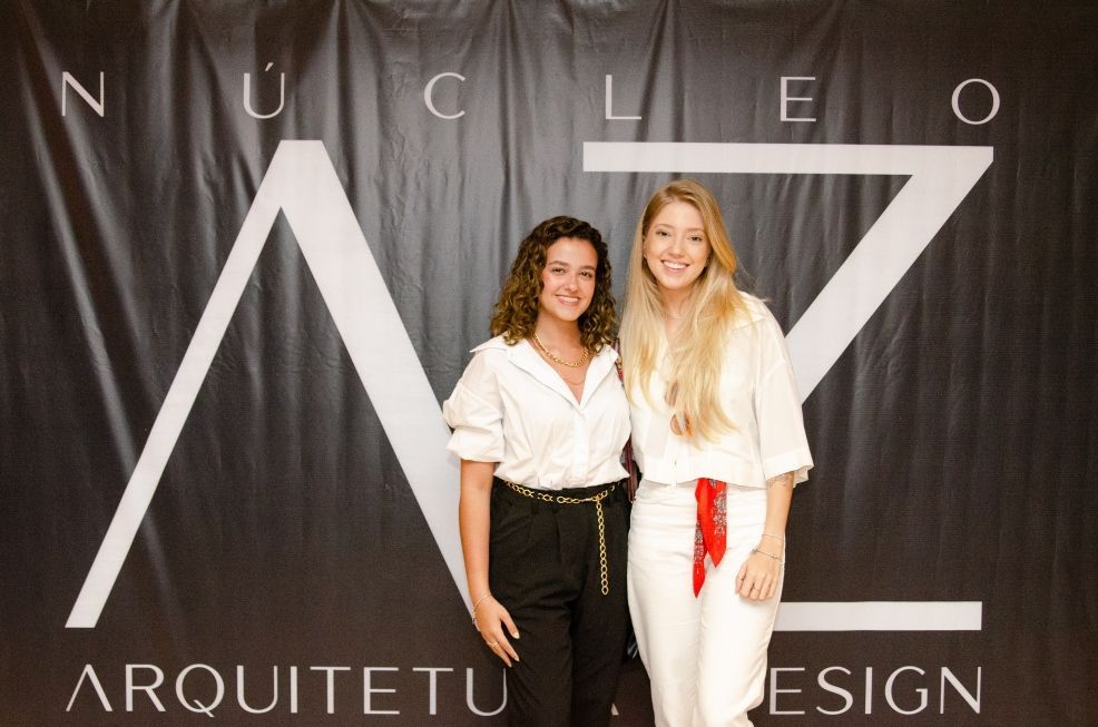 Duas mulheres posam para uma foto em frente a uma placa que diz arquitetu design