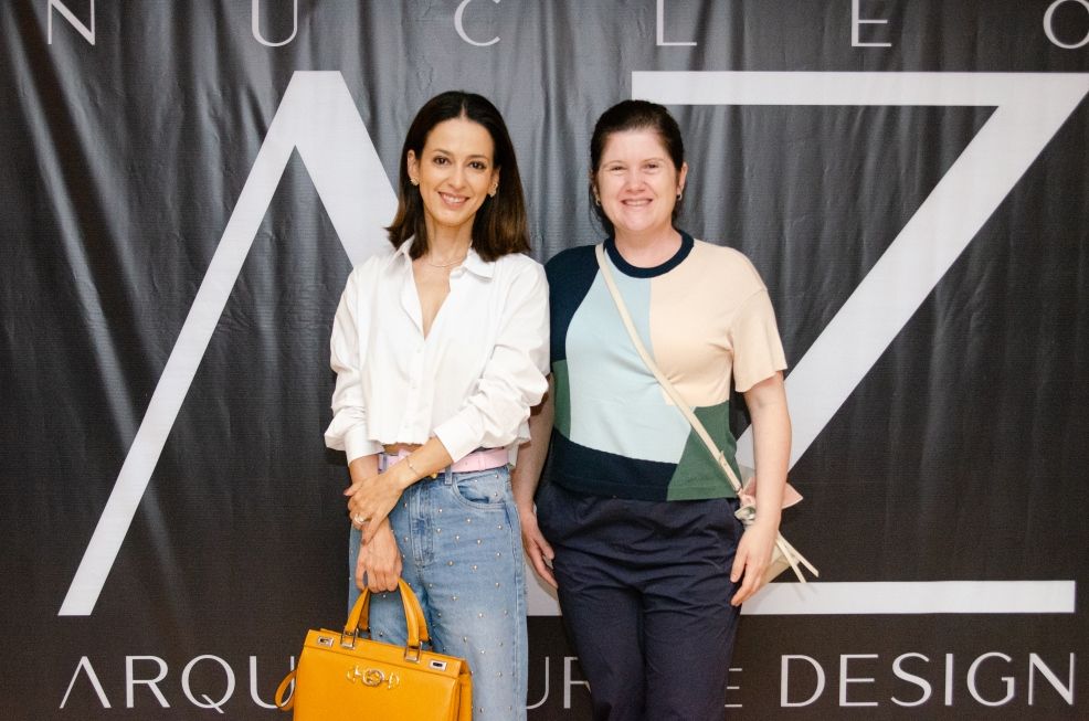 Duas mulheres posam para uma foto em frente a uma placa que diz design