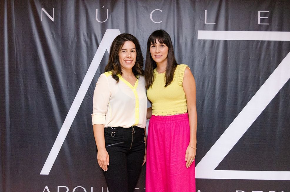 Duas mulheres estão posando para uma foto em frente a uma cortina preta.